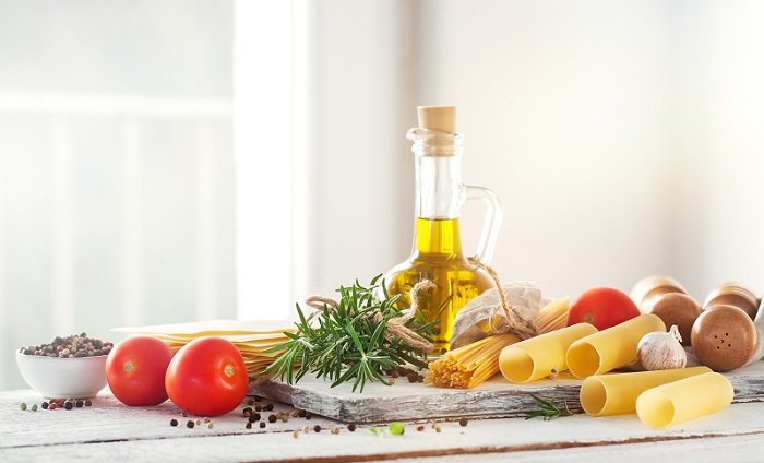 Healthy ingredients on a kitchen table - spaghetti, olive oil, tomatoes, spices and fresh italian herbs on a shiny background. Cooking or healthy life concept, horizontal