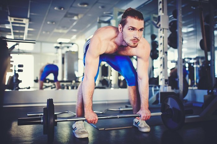 Portrait of sporty topless man weightlifting in gym